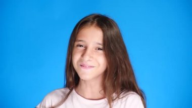 Uzun saçlı sevimli heyecan çekici kız portresi. mavi arka plan üzerinde dururken gülüyor. 4 k, yavaş hareket, yakın çekim