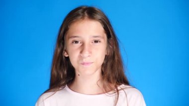 Uzun saçlı sevimli heyecan çekici kız portresi. mavi arka plan üzerinde dururken gülüyor. 4 k, yavaş hareket, yakın çekim