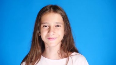 Uzun saçlı sevimli heyecan çekici kız portresi. mavi arka plan üzerinde dururken gülüyor. 4 k, yavaş hareket, yakın çekim.