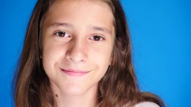 Uzun saçlı sevimli heyecan çekici kız portresi. mavi arka plan üzerinde dururken gülüyor. 4 k, yavaş hareket, yakın çekim