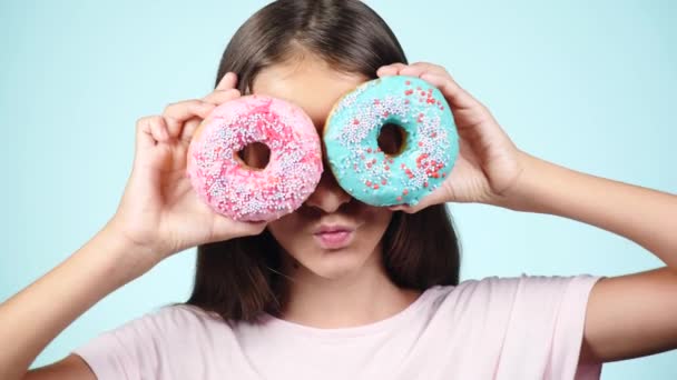 Fecha a porta. retrato de uma garota engraçada com cabelos longos, se divertindo com donuts coloridos contra o rosto. Expressões, conceito de dieta, cor de fundo — Vídeo de Stock