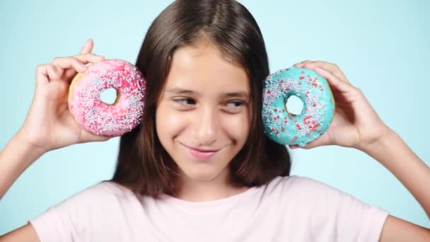 Close-up. Portret van een grappig meisje met lange haren, plezier maken met kleurrijke donuts tegen haar gezicht. Expressies, dieet concept, achtergrondkleur — Stockvideo