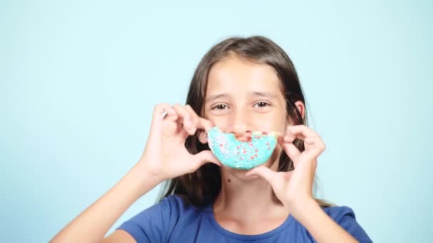 Close-up. Portret van een grappig meisje met lange haren, plezier maken met kleurrijke donuts tegen haar gezicht. Expressies, dieet concept, achtergrondkleur — Stockvideo