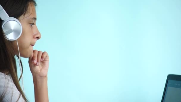 Hintergrund aus nächster Nähe. Ein hübsches Teenager-Mädchen auf farbigem Hintergrund blickt mit weißen Kopfhörern auf den Laptop-Bildschirm. Zeitlupe, 4k — Stockvideo