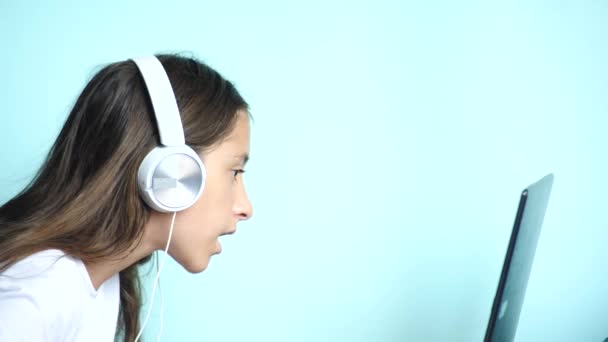 クローズ アップの背景。白いヘッドフォンで色付きの背景に美しい十代の少女は、ノート パソコンの画面に見えます。スローモーション、4 k — ストック動画