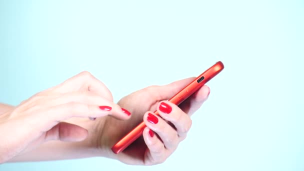 Közelkép, női kezek piros manikűr használ egy smartphone színes háttéren. 4k, lassú mozgású felvétel — Stock videók