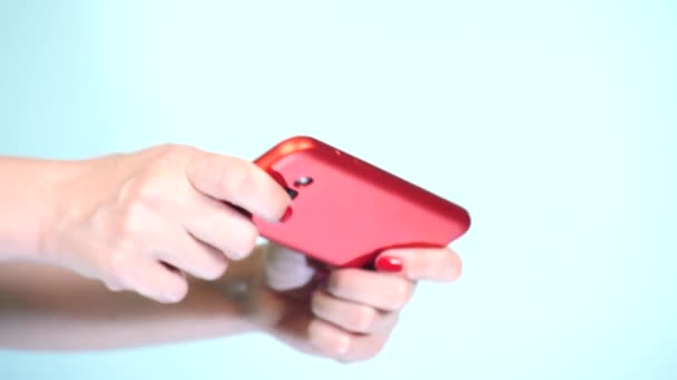 gros plan, les mains féminines avec manucure rouge utilisent un smartphone sur un fond coloré. 4k, tir au ralenti 