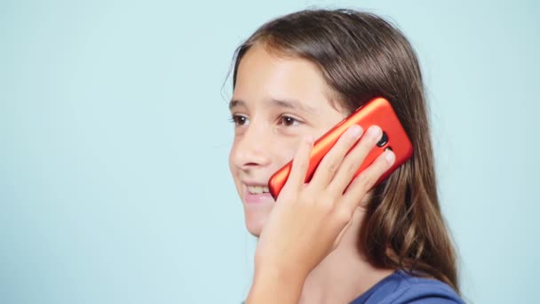 Primer plano, una adolescente sosteniendo un teléfono inteligente rojo cerca de la oreja. La chica está hablando por teléfono. 4k, cámara lenta. color de fondo — Vídeos de Stock