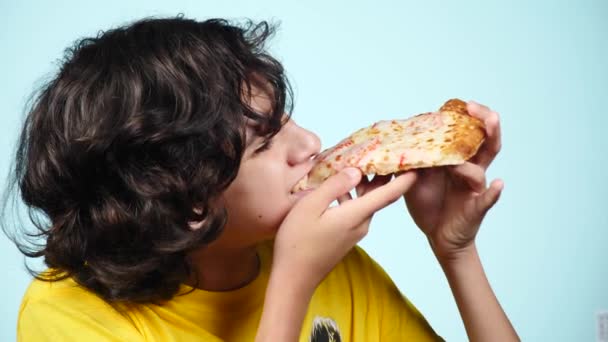 Pizza. Niño feliz adolescente sosteniendo pizza. El concepto de nutrición. el chico está comiendo pizza. Hombre rizado sonriente con una deliciosa pizza. Pizzería de publicidad. sobre un fondo azul. 4k cámara lenta — Vídeo de stock