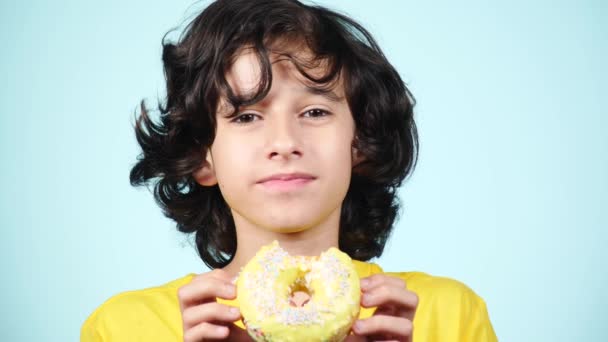 Closeup. portrait of a funny guy with curly hairs, having fun with colorful donuts against his face. Expressions, diet concept, background color. 4k — Stock Video