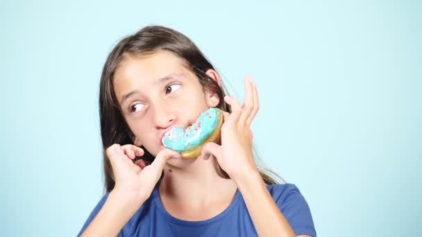 Primer plano. retrato de una chica divertida con pelos largos, divirtiéndose con rosquillas de colores contra su cara. Expresiones, concepto de dieta, color de fondo — Vídeos de Stock