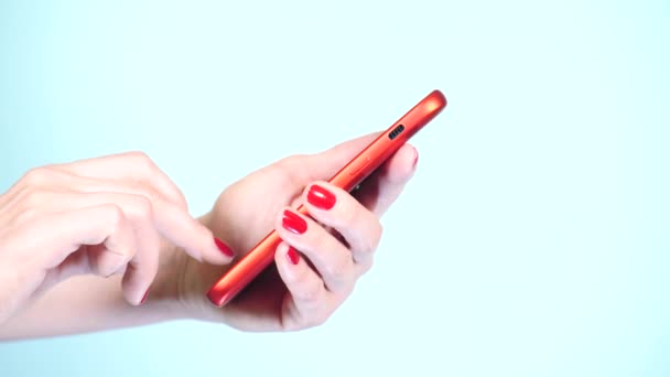 Close-up, mãos femininas com manicure vermelho usar um smartphone em um fundo colorido. 4k, tiro em câmera lenta — Vídeo de Stock