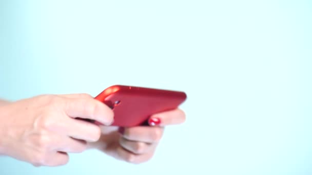 Close-up, mãos femininas com manicure vermelho usar um smartphone em um fundo colorido. 4k, tiro em câmera lenta — Vídeo de Stock