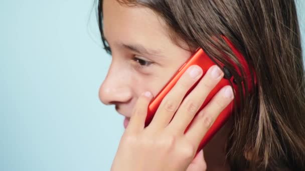 Primo piano, un'adolescente con uno smartphone rosso vicino all'orecchio. La ragazza sta parlando al telefono. 4k, rallenta. colore di sfondo — Video Stock