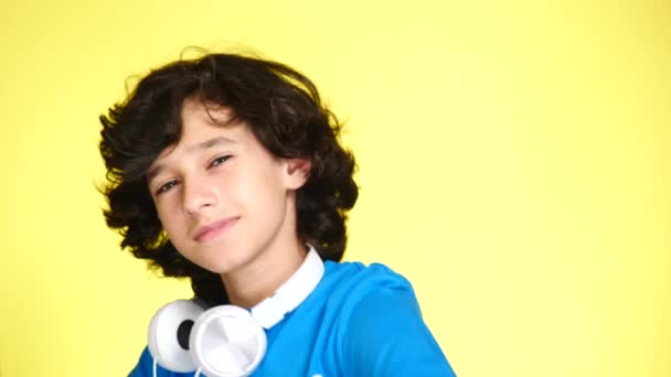 Niño adolescente con auriculares y teléfono móvil escuchando música en el fondo de color. primer plano, 4k, cámara lenta . — Vídeo de stock