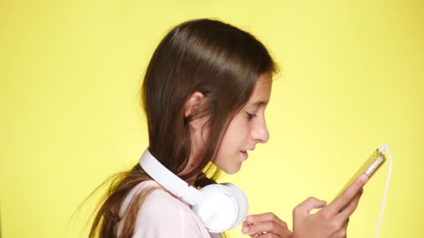 Tienermeisje met hoofdtelefoons en mobiele telefoon luisteren naar muziek op de achtergrond in kleur. Close-up, 4k, slow-motion. maakt selfi op smartphone — Stockvideo