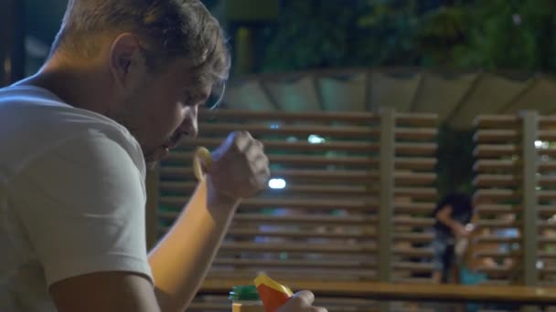 Печальный человек, сидящий ночью в ресторане быстрого питания, ест картошку фри в одиночестве. 4k — стоковое видео