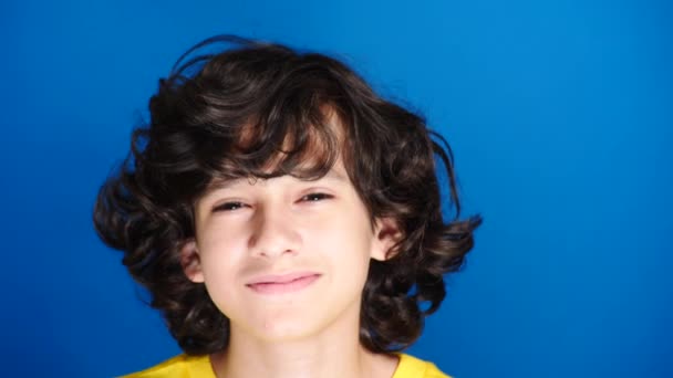 Schattige curly-haired jongen de tiener ziet er in de camera lachen. 4 k, slow motion, close-up. kleur achtergrond. — Stockvideo