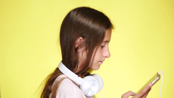 色の背景に音楽を聴く携帯電話とヘッドフォンの 代の少女 クローズ アップ スローモーション — ストック動画