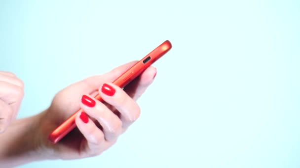 Close-up, mãos femininas com manicure vermelho usar um smartphone em um fundo colorido. 4k, tiro em câmera lenta — Vídeo de Stock