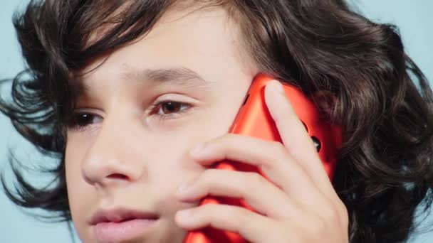 Крупный план, мальчик-подросток держит красный смартфон рядом с ухом. Парень разговаривает по телефону. 4К, замедленная съемка. Цвет фона — стоковое видео