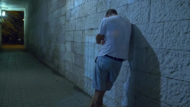 Un ivrogne marche seul la nuit à travers un tunnel piétonnier. 4k . — Video