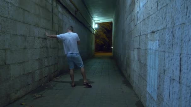 Een dronken man loopt alleen 's nachts via een voetgangerstunnel. 4k. — Stockvideo