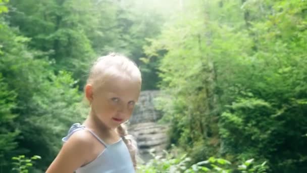 Little girl model in a beautiful blue dress posing against a waterfall in the forest. 4k, slow motion. — Stock Video