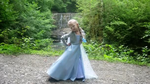 Modello bambina in un bellissimo vestito blu in posa contro una cascata nella foresta. 4k, rallentatore . — Video Stock