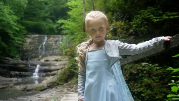 Kleine meisje model in een mooie blauwe jurk poseren tegen een waterval in het forest. 4k, slow-motion. — Stockvideo