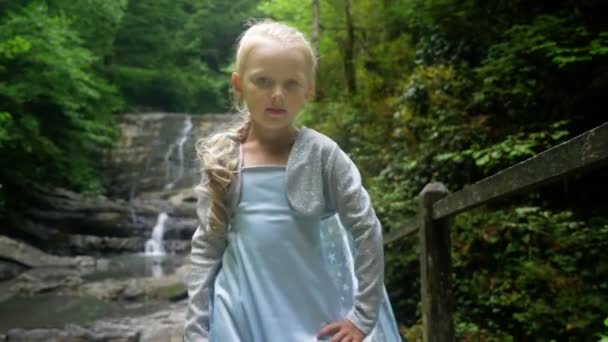 Little girl model in a beautiful blue dress posing against a waterfall in the forest. 4k, slow motion. — Stock Video