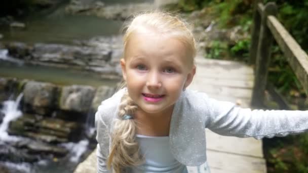 Close-up. portrait of a little girl model in a beautiful blue dress, posing against a waterfall in a forest. makes funny faces. 4k, slow motion. — Stock Video