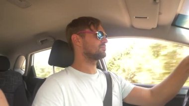 Güneş gözlüklü genç yakışıklı bir adam bir araba dağ manzaralı bir otoyol boyunca yüksek hızda yol açar. 4k, ağır çekim