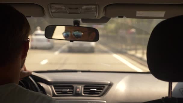 Un joven guapo con gafas de sol está conduciendo un coche por la ciudad. reflejo en el espejo retrovisor. 4k, cámara lenta — Vídeo de stock