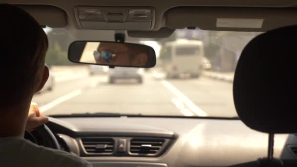 Ein junger gutaussehender Mann mit Sonnenbrille fährt mit einem Auto durch die Stadt. Spiegelung im Rückspiegel. 4k, Zeitlupe — Stockvideo