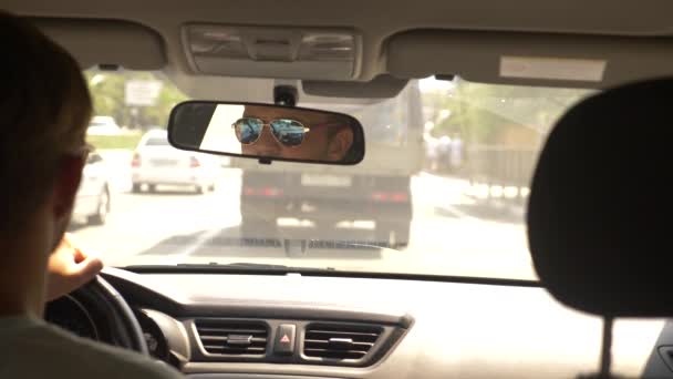 Een knappe jongeman in zonnebril is het besturen van een auto rond de stad. reflectie in de achteruitkijkspiegel. 4k, slow-motion — Stockvideo