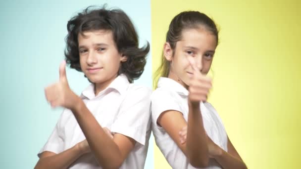 Retratos de niños en uniforme escolar sobre un fondo de color. Niños graciosos. Hermana y hermano. concepto de escolaridad. Miran a la cámara y muestran el pulgar hacia arriba. espacio de copia — Vídeos de Stock