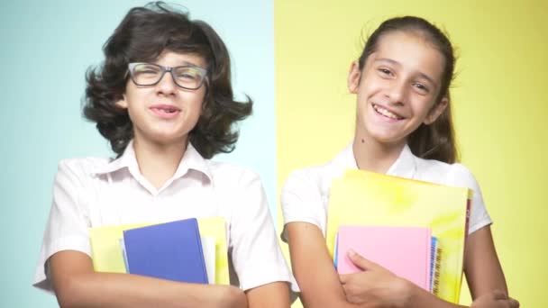Çocuklar okulda bir renkli arka plan üzerinde üniforma portreleri. Komik çocuk. Kız ve erkek kardeş. öğrenme kavramı. Kameraya bakarak ve gülümseyen kitaplar burada tutuyorlar. kopya alanı — Stok video