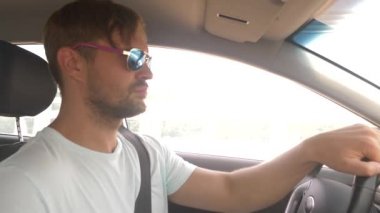 Güneş gözlüklü genç yakışıklı bir adam bir araba dağ manzaralı bir otoyol boyunca yüksek hızda yol açar. 4k, ağır çekim