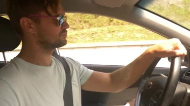 Güneş gözlüklü genç yakışıklı bir adam bir araba dağ manzaralı bir otoyol boyunca yüksek hızda yol açar. 4k, ağır çekim