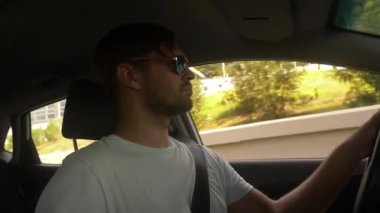 Güneş gözlüklü genç yakışıklı bir adam bir araba dağ manzaralı bir otoyol boyunca yüksek hızda yol açar. 4k, ağır çekim