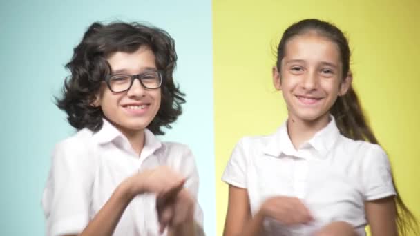 Portretten van kinderen in school uniform op een gekleurde achtergrond. Grappige kinderen. Zus en broer. concept van leren. Ze kijken naar de camera, lachen en dansen. — Stockvideo
