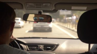 Güneş gözlüklü genç yakışıklı bir adam bir araba şehir etrafında sürüş. dikiz aynası yansıması. 4k, ağır çekim