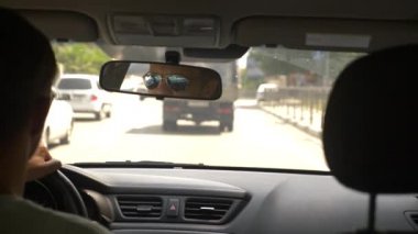 Güneş gözlüklü genç yakışıklı bir adam bir araba şehir etrafında sürüş. dikiz aynası yansıması. 4k, ağır çekim