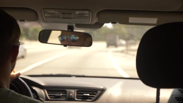 Um jovem bonitão de óculos de sol está dirigindo um carro pela cidade. reflexão no espelho retrovisor. 4k, câmera lenta — Vídeo de Stock