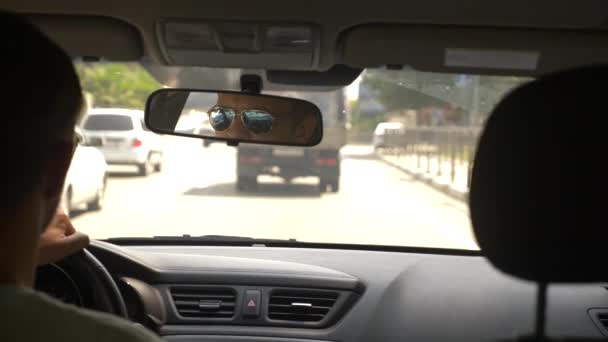 Um jovem bonitão de óculos de sol está dirigindo um carro pela cidade. reflexão no espelho retrovisor. 4k, câmera lenta — Vídeo de Stock