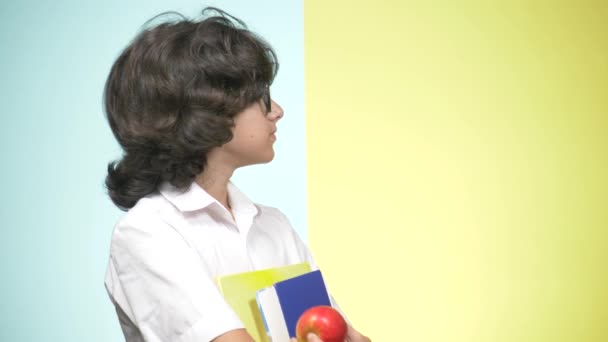 Porträtt av en tonårig pojke i skoluniform som på en färgad bakgrund. Rolig kille. begreppet lärande. En tonåring håller böcker tittar på kameran och leende. kopia utrymme — Stockvideo
