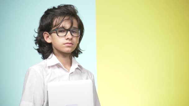 Portraits d'une adolescente en uniforme scolaire et lunettes sur fond coloré. Un drôle de type. concept d'apprentissage. Un adolescent tient un ordinateur portable, regarde la caméra, sourit et fait des grimaces drôles — Video