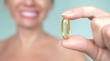 Sağlıklı bir diyet yemek. Güzel bir balık yağı hapı elinde tutan genç kadın gülümsüyor. Portre. kapsül alıyor. Vitamin ve diyet takviyeleri. mavi arka plan, bulanıklık, 4k
