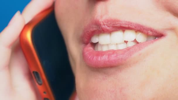 Close-up, vrouwelijke lippen zonder make-up praten over een rode mobiele telefoon, tegen een blauwe achtergrond. 4k, slow-motion — Stockvideo